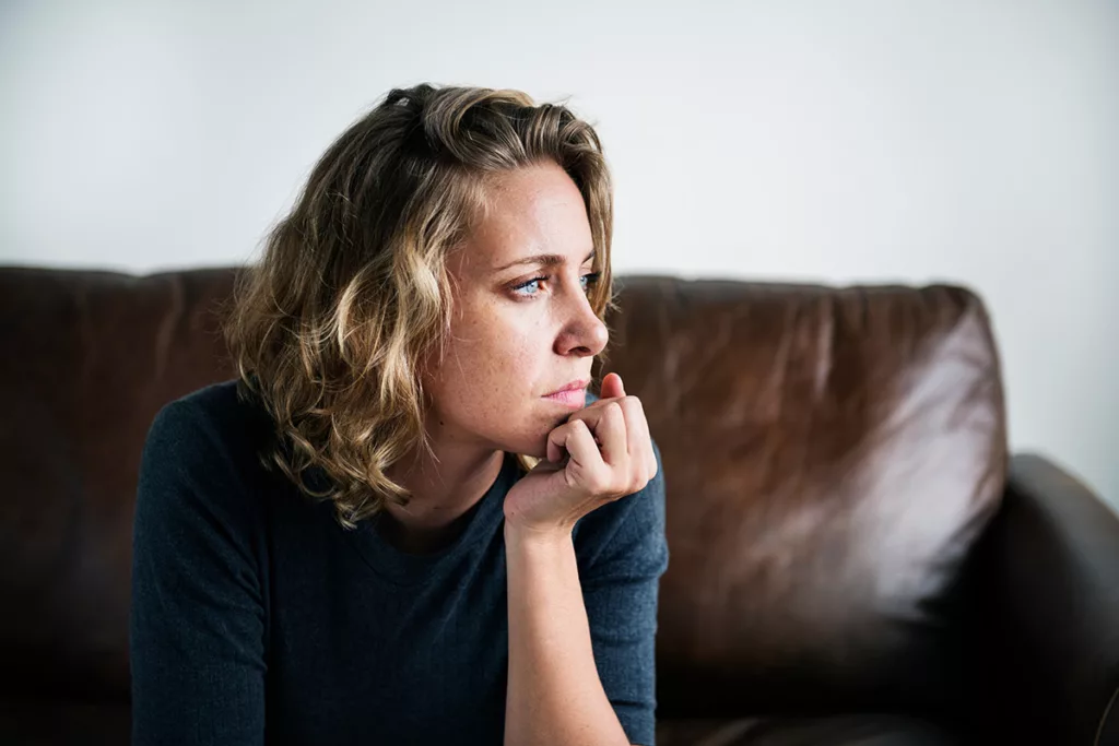 Woman looking sad on couch with hand on chin. 